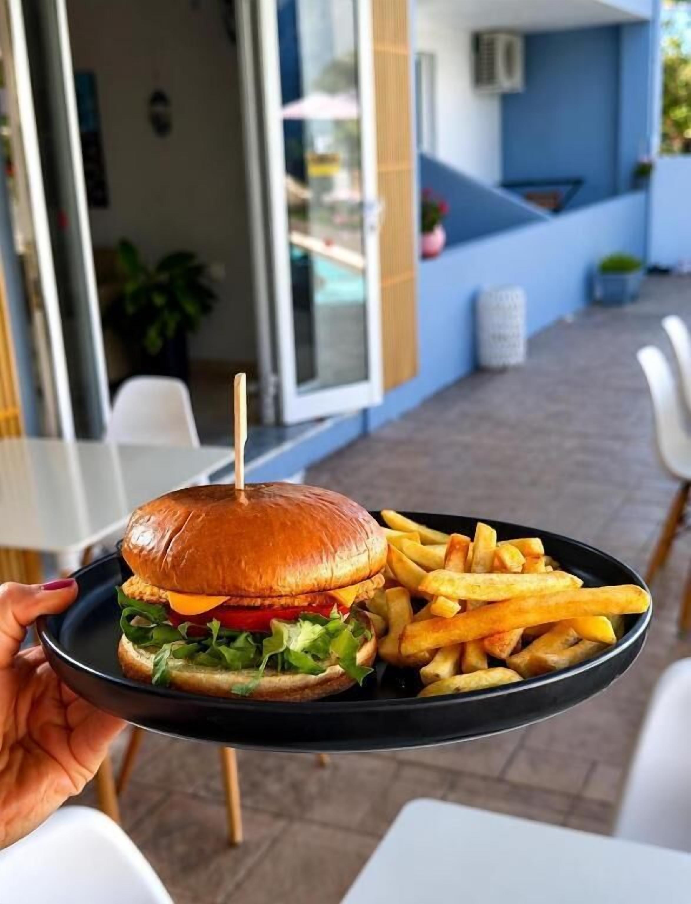 Una persona sosteniendo una bandeja con una hamburguesa y papas fritas.