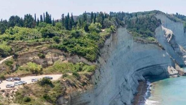 Acantilado costero con playa y un camino pavimentado.