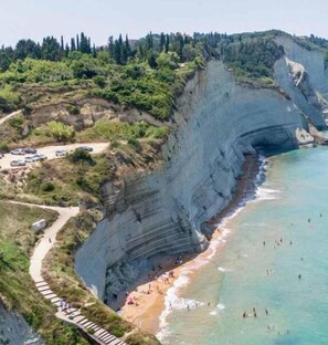 A coastal cliffside with a beach and a paved walkway. - Melitsa corfu hotel  (Corfu)