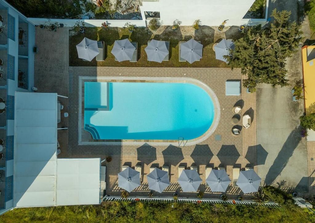 An aerial view of a hotel with a swimming pool, sun loungers, and umbrellas.