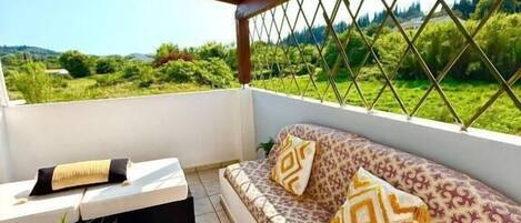 A covered outdoor seating area with a sofa, cushions, a small table, and a potted plant.
