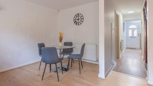 Et spiseområde med et rundt bord, fire stole, et vægur og en radiator.