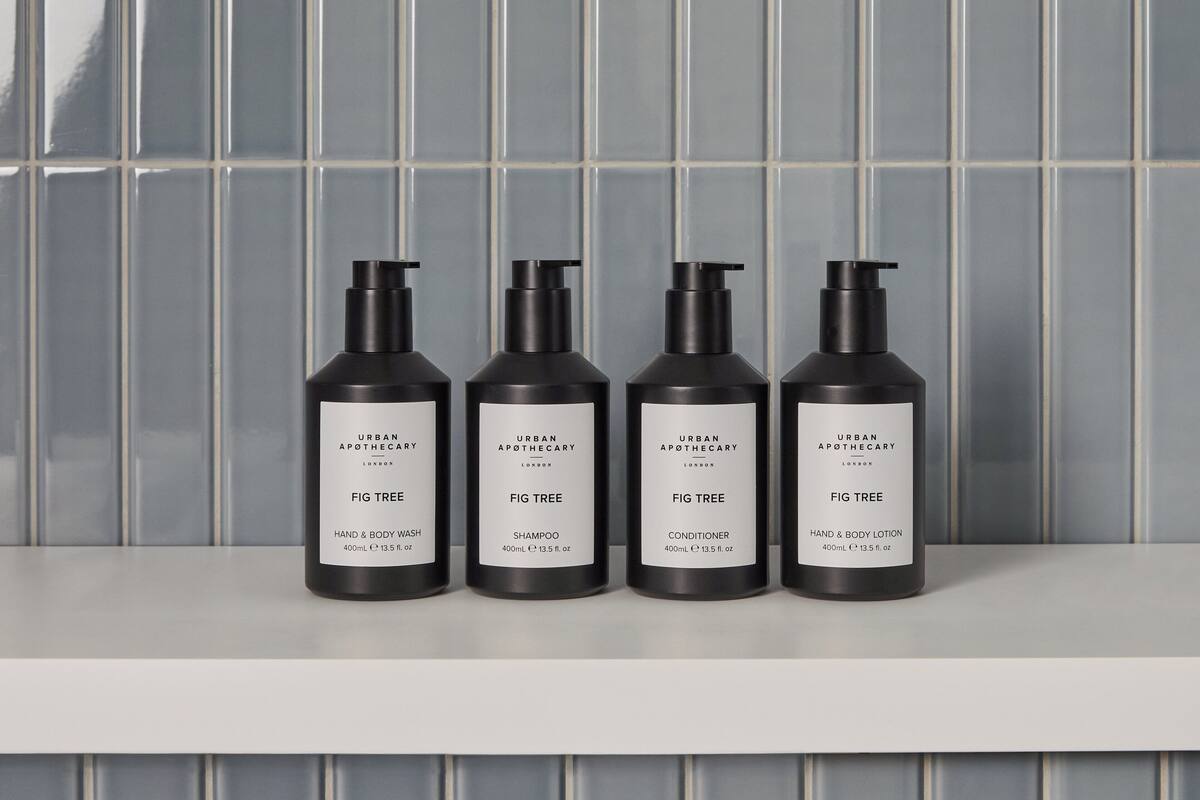 Quatro frascos pretos de produtos Urban Apothecary Fig Tree sobre uma prateleira branca, em frente a uma parede azulejada.