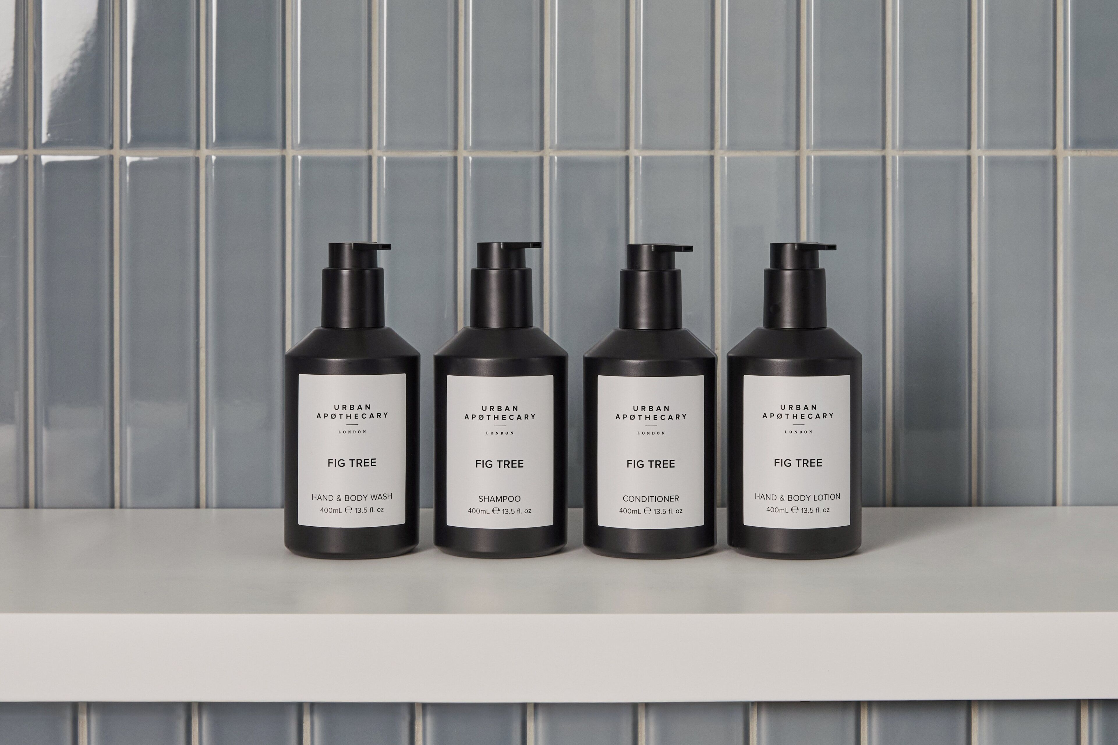 Four black bottles of Urban Apothecary Fig Tree products on a white shelf against a tiled wall.