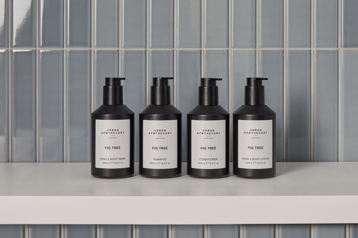 Four black bottles of Urban Apothecary Fig Tree products on a white shelf against a tiled wall.