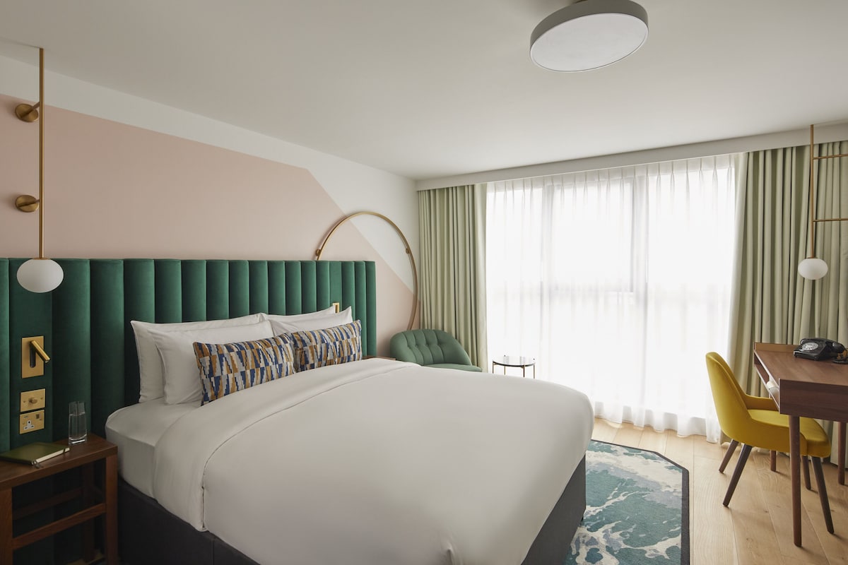 A hotel room with a large bed, a desk with a telephone, a chair, and a lamp.