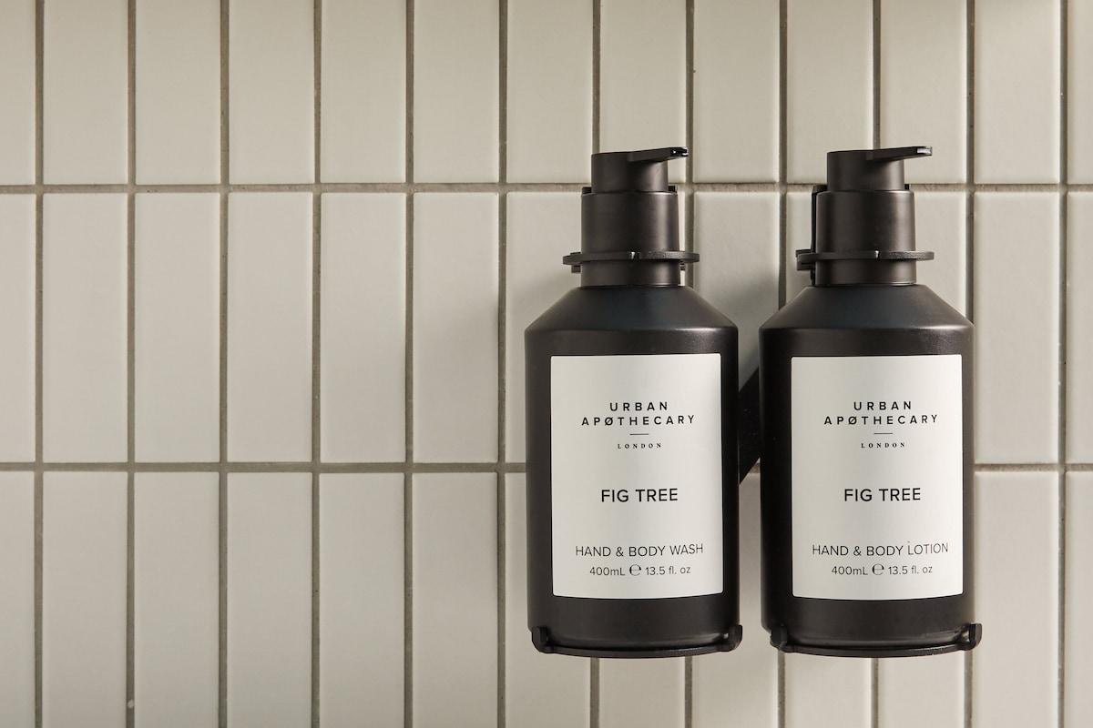 Two black bottles with white labels, labeled 'URBAN APOTHECARY LONDON FIG TREE HAND & BODY WASH' and 'URBAN APOTHECARY LONDON FIG TREE HAND & BODY LOTION,' against a tiled wall.
