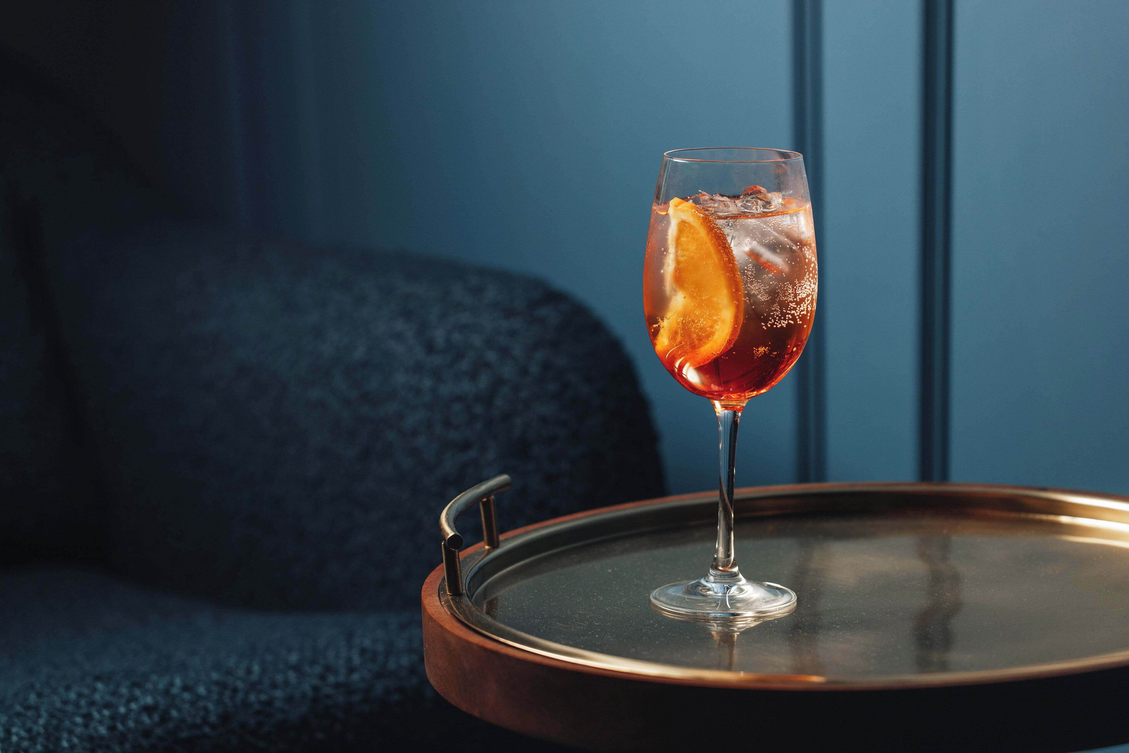 A glass of red beverage with an orange slice on a copper tray.