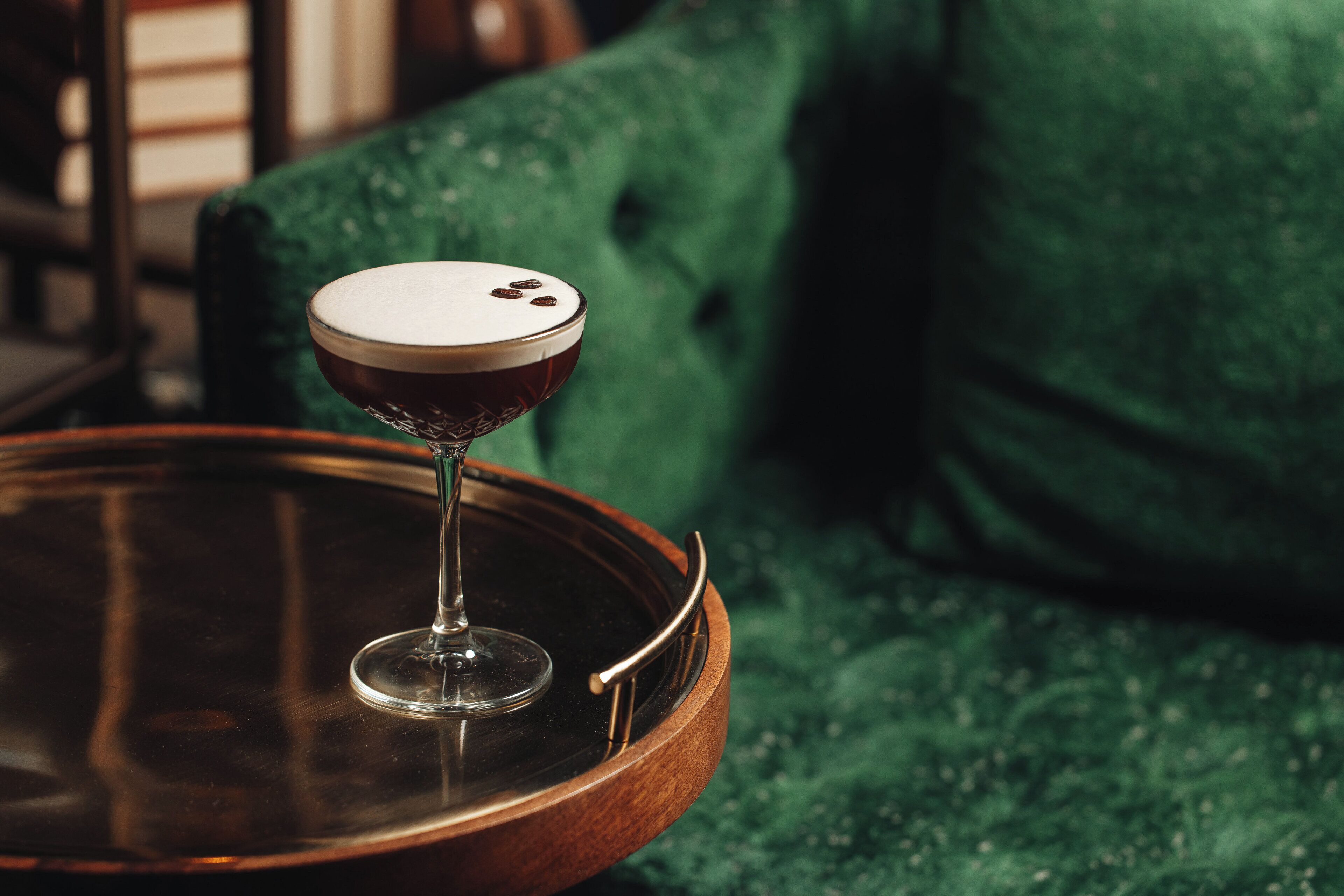 A cocktail glass with a frothy top on a wooden tray, placed on a green textured surface.