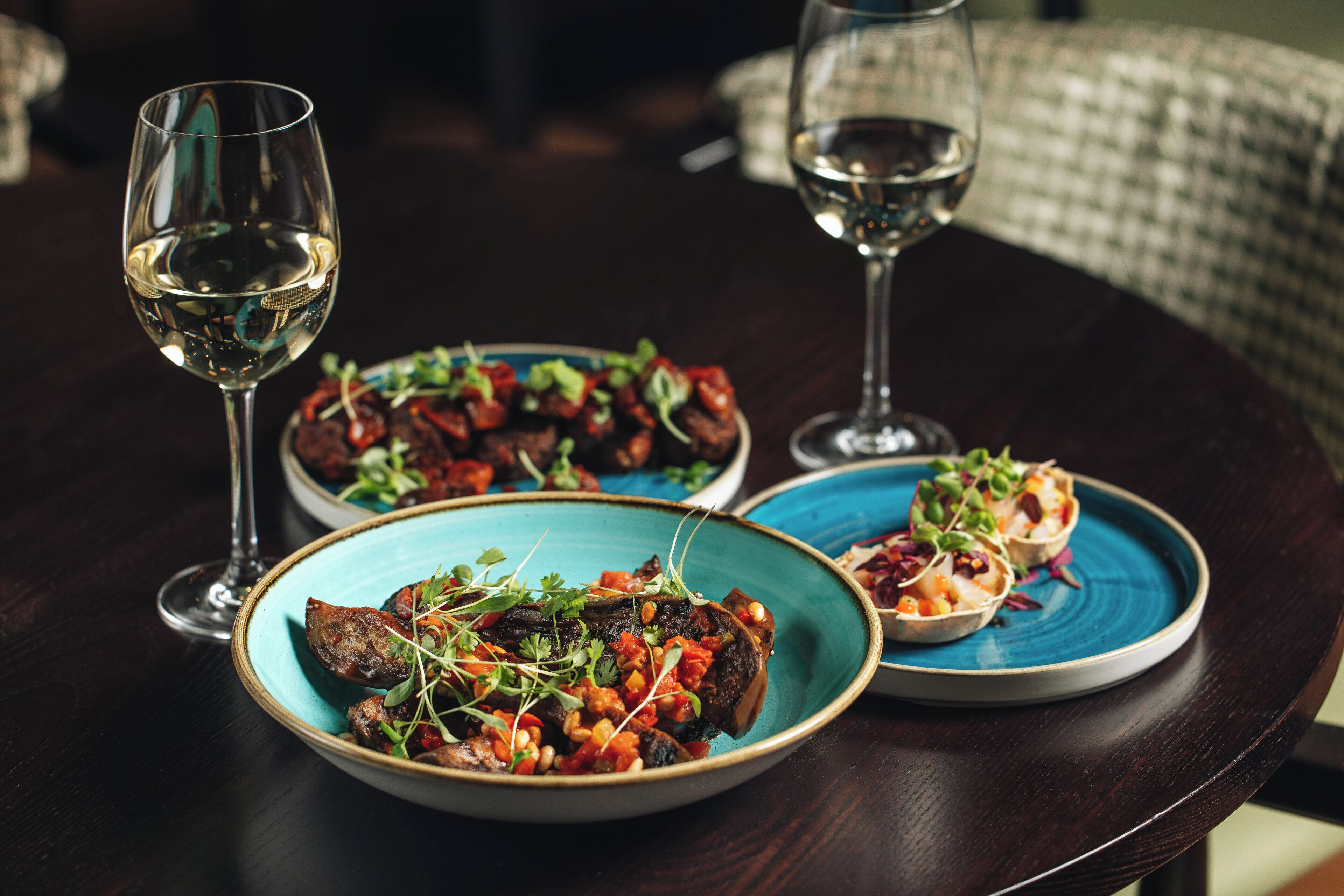 A table with three plates of food and two glasses of white wine.