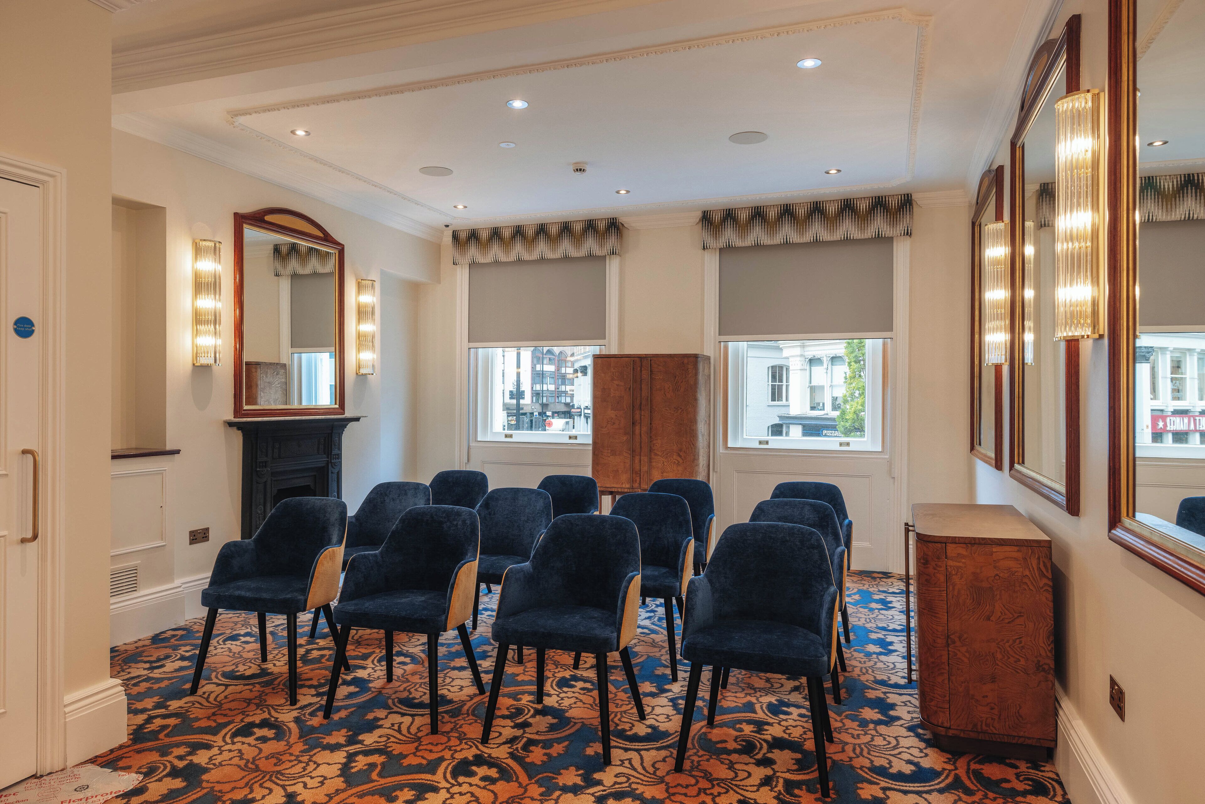 A conference room with a patterned carpet, rows of chairs, a fireplace, and large windows with curtains.