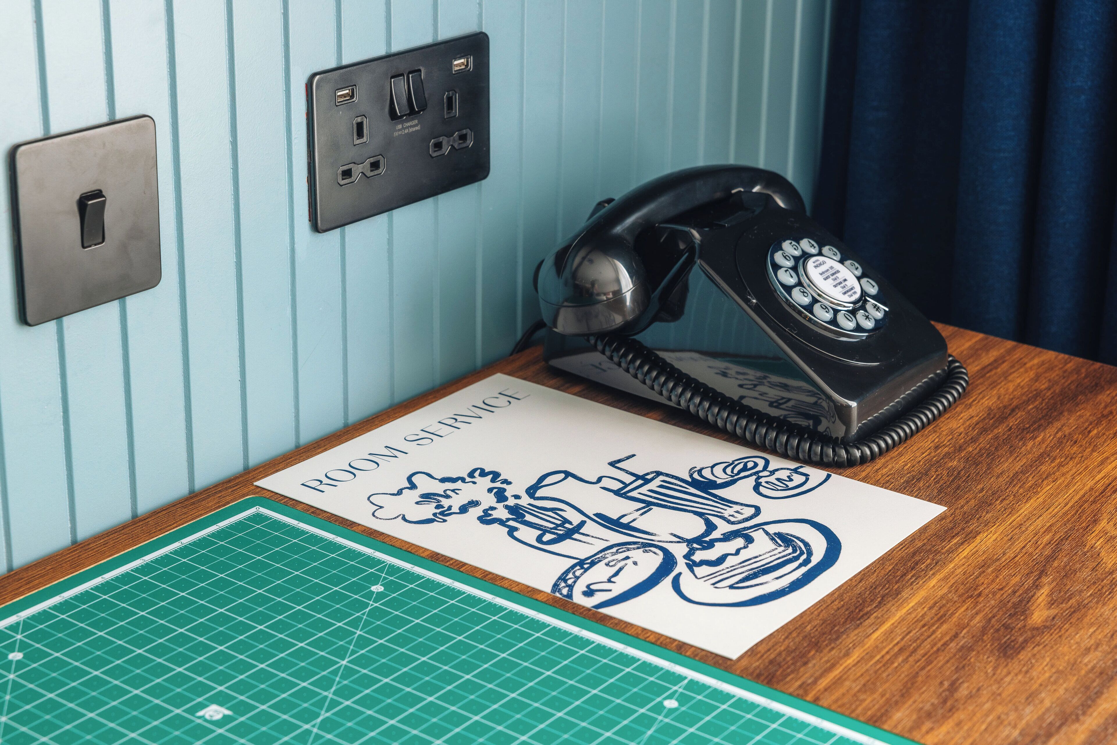 A room with a vintage rotary phone, a light switch, and a cutting mat on the table.