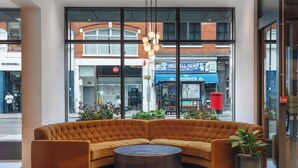 A corner sofa with a round coffee table, large windows, and potted plants. - Hotel Indigo London Clerkenwell by IHG (London)
