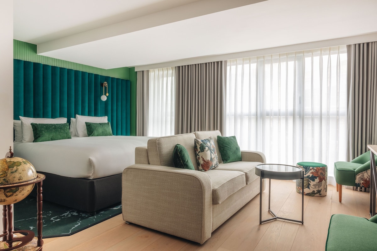 A hotel room with a bed, a sofa, a small table, and a chair.