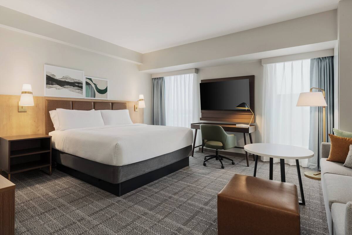 A hotel room with a bed, desk, TV, and seating area.