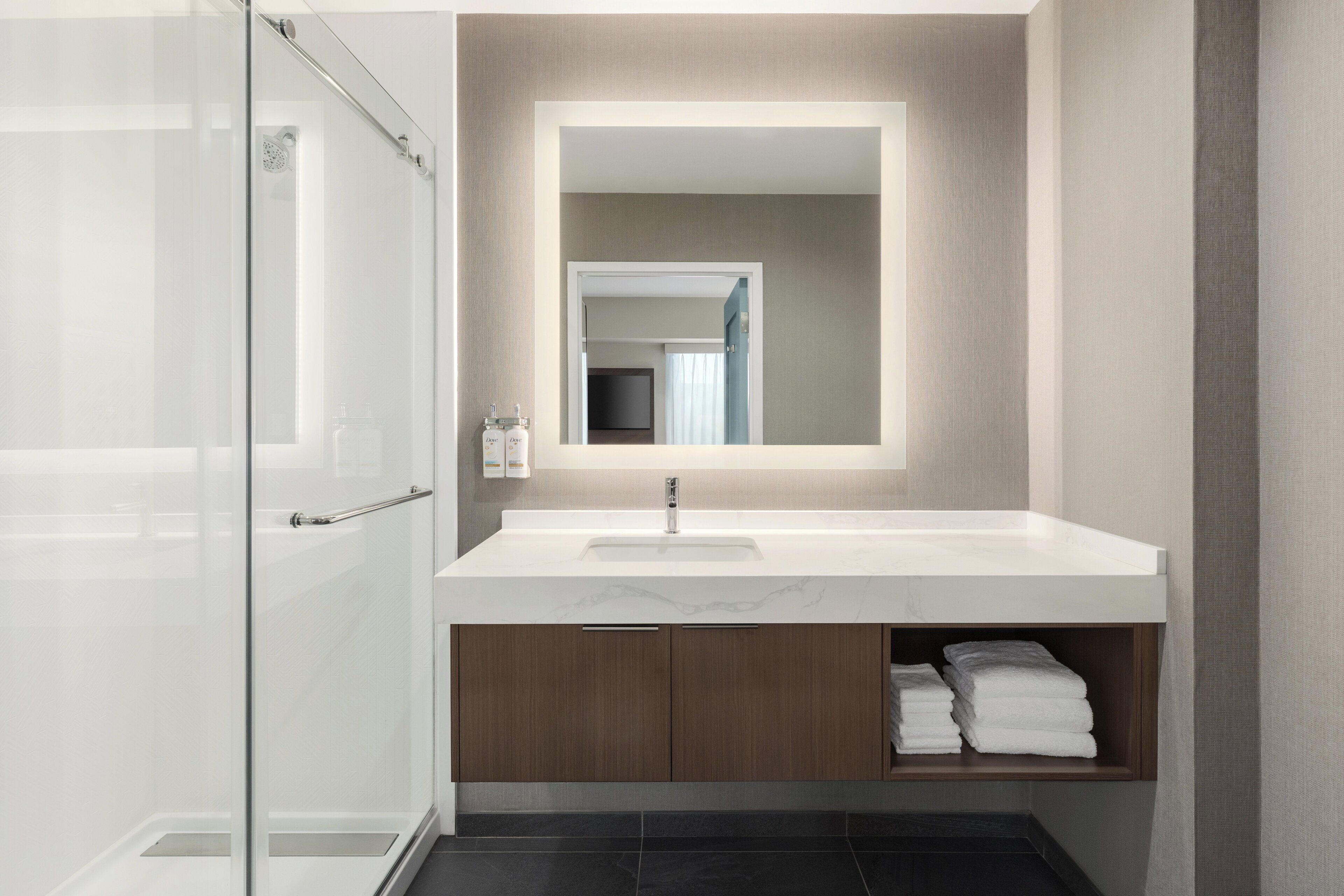 Une salle de bain moderne avec une douche à l’italienne en verre, un lavabo blanc et des meubles en bois.