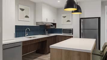 A modern kitchen with white cabinetry, a central island, a stainless steel refrigerator, and a black pendant light.
