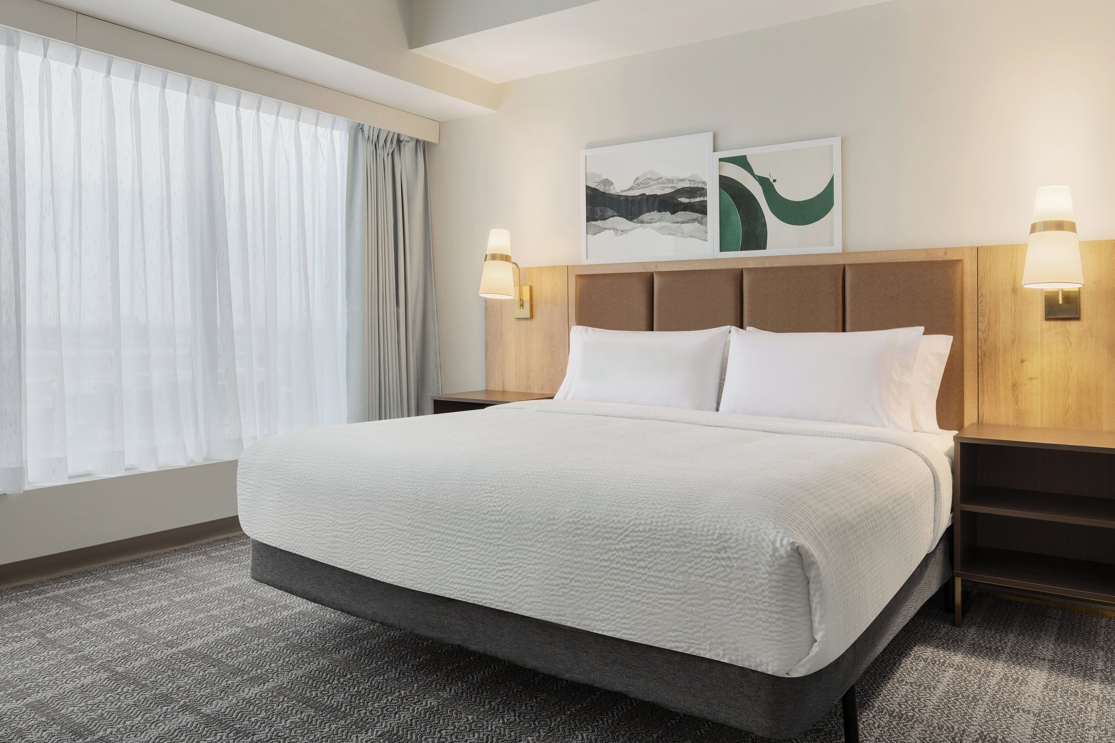 Habitación de hotel con una cama grande, dos lámparas de pared, cabecera y una obra de arte en la pared.