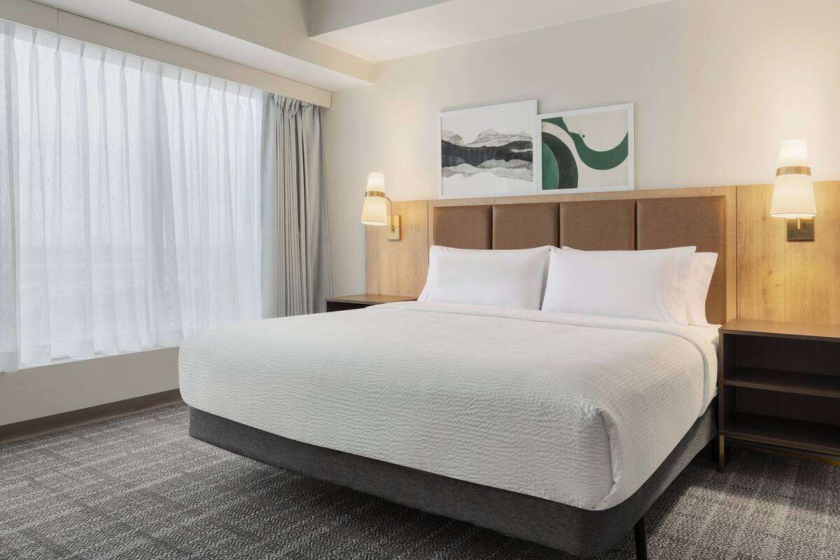 A hotel room with a large bed, two wall-mounted lamps, a headboard, and artwork on the wall.