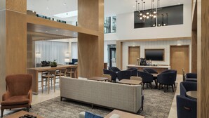 Un vestíbulo espacioso con techo alto, una zona de estar central y una cocina moderna a la vista.