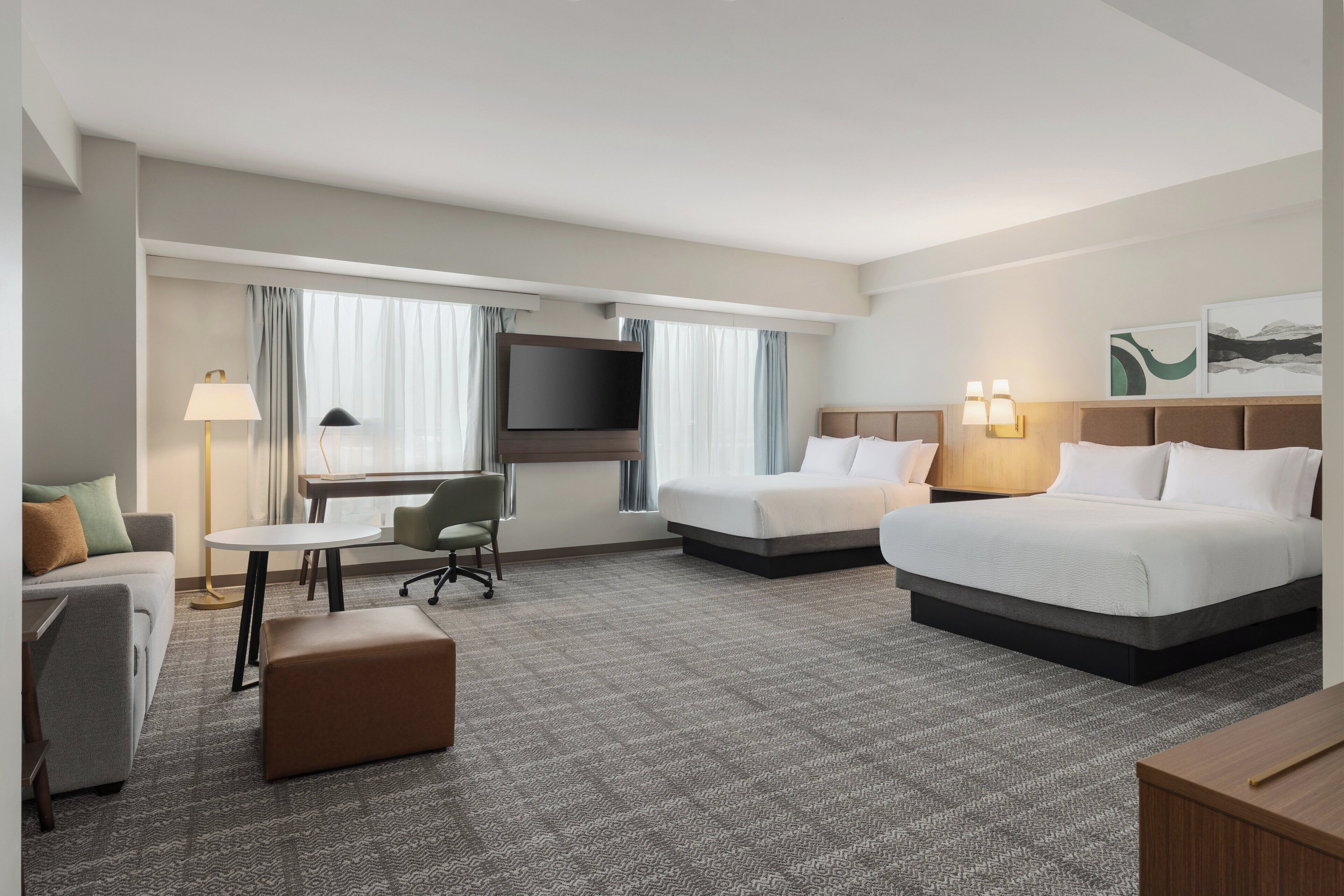 A hotel room with two beds, a desk, a chair, a TV, and a window with curtains.