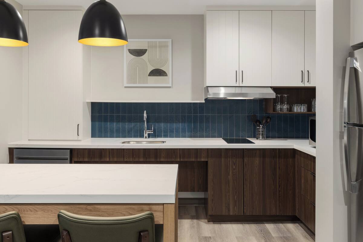 Una cocina moderna con armarios blancos, un protector contra salpicaduras azul y un refrigerador de acero inoxidable.