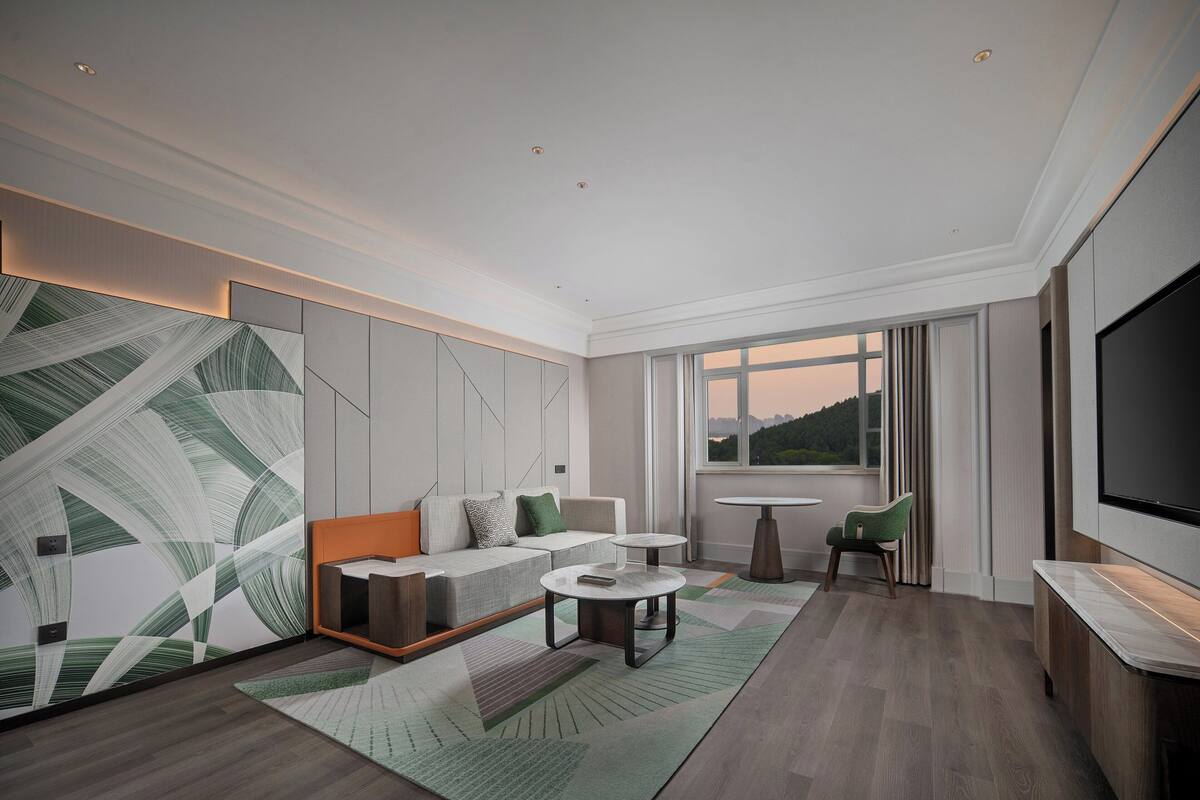 Ein modernes Hotelzimmer mit einer Sitzecke, zwei kleinen Tischen, einem Fernseher und einem großen Fenster mit Blick.