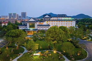A large hotel with traditional architecture, surrounded by lush greenery and a view of a city skyline.