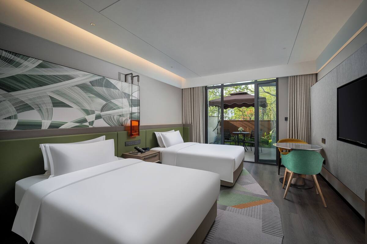 Ein Hotelzimmer mit zwei Betten, einem Fernseher, einem Tisch mit Stühlen und Blick ins Freie.