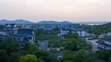A traditional Chinese architectural style building complex with multiple structures, surrounded by lush greenery and a hilly landscape in the background.