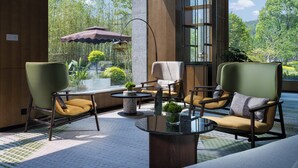 A modern outdoor seating area with chairs and a table, large windows offering a view of greenery and trees. - Holiday Inn Xuzhou Yunquan by IHG (Xuzhou)