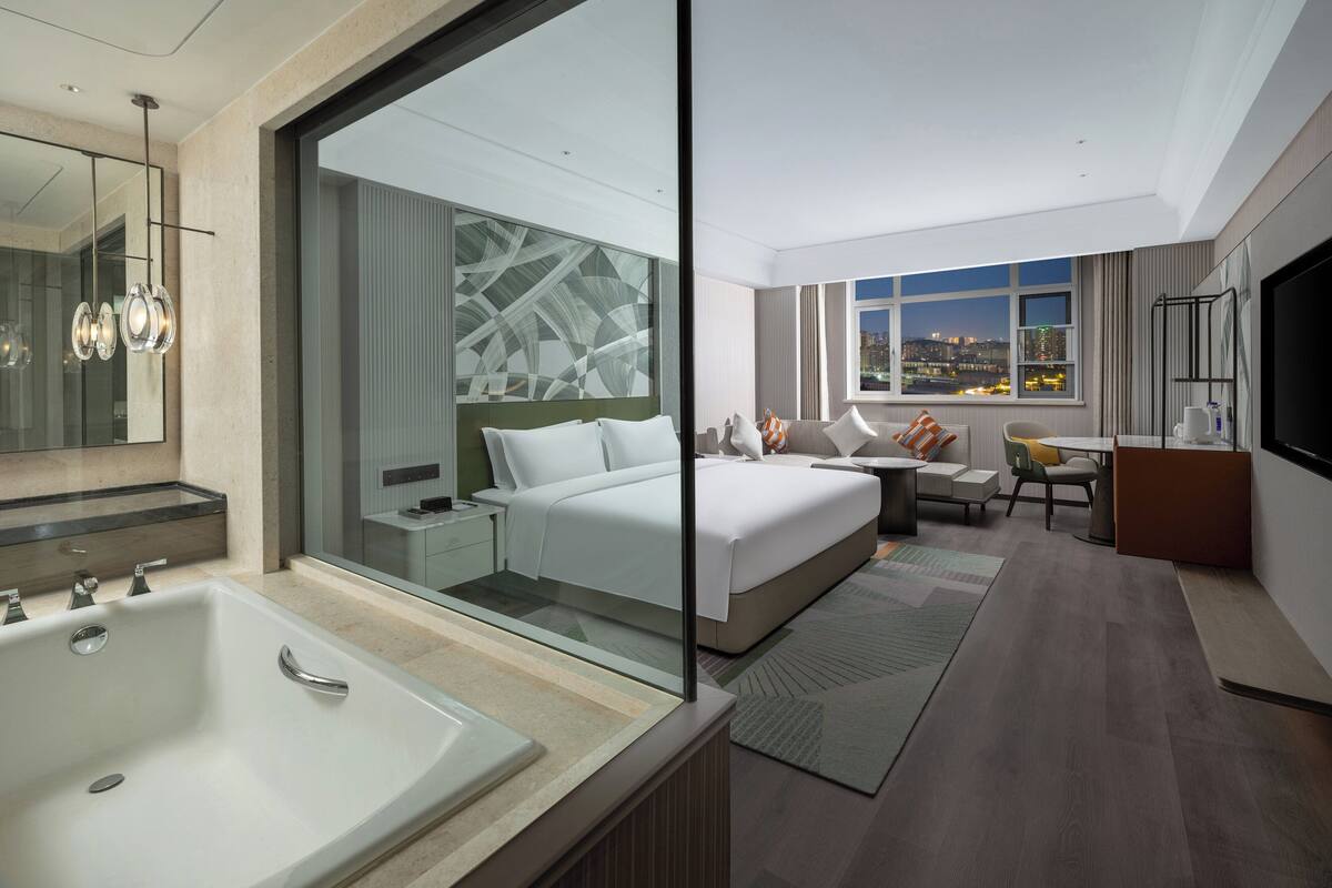 Ein modernes Hotelzimmer mit einem großen Bett, einer Sitzecke, einem Schreibtisch und einem Badezimmer mit einer großzügigen Badewanne.