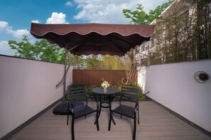Un patio con mesa y sillas bajo una marquesina, rodeado por un muro bajo y vegetación.