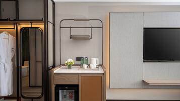 A modern hotel room with a minibar, a TV, a mirror, and a robe rack.