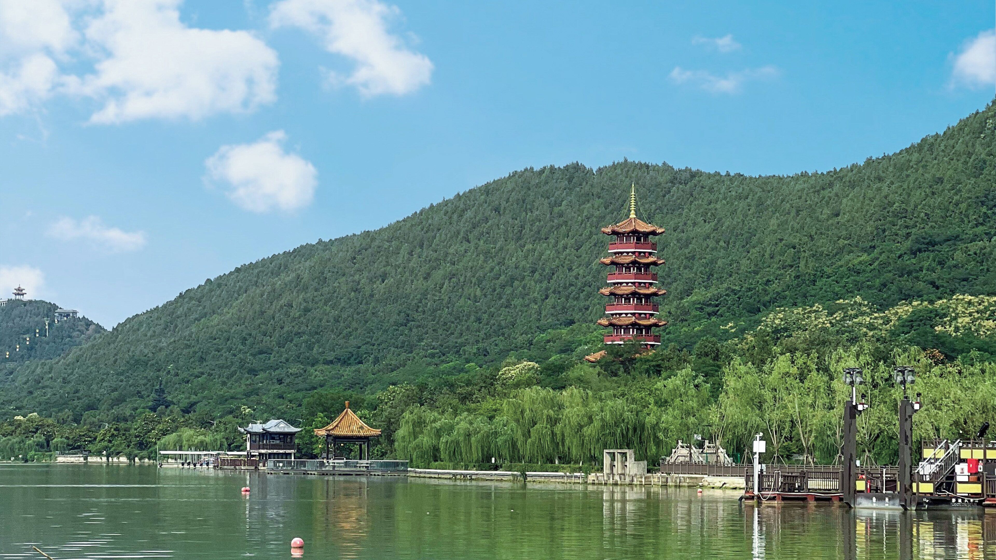 A pagoda-style tower on a hill with a lake in the foreground.