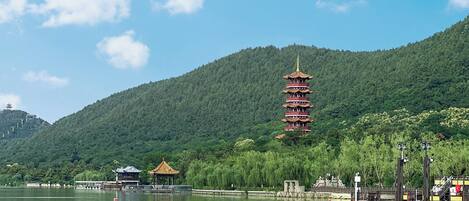 A pagoda-style tower on a hill with a lake in the foreground.