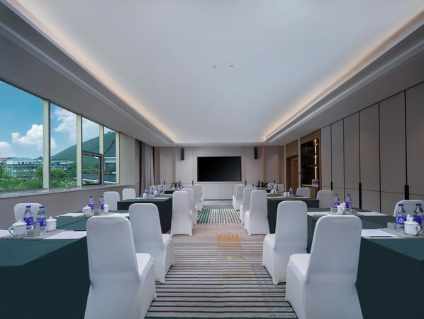 Un salón de conferencias con una gran mesa, sillas blancas, un televisor de pantalla plana y vistas a edificios y colinas.