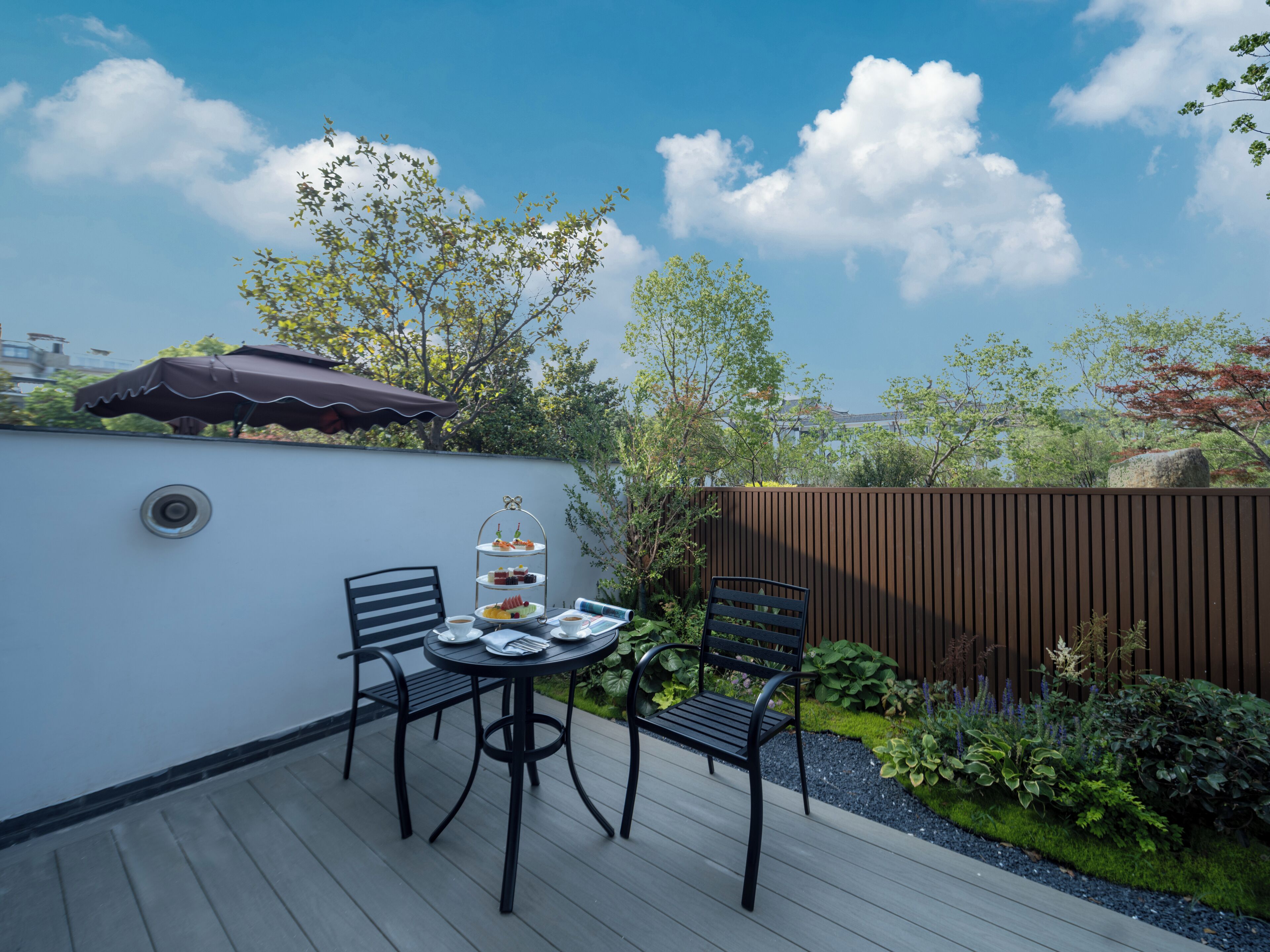 A patio with a table set for a tea service, surrounded by chairs and a decorative umbrella.