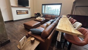 Una sala de estar moderna con una mesa de madera alargada, sofás de cuero, una chimenea y un televisor montado en la pared.