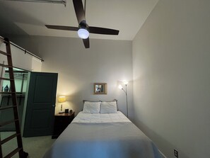 Cozy retreat with a single bed, nightstand, and ceiling fan, plus a ladder leading to a loft area.