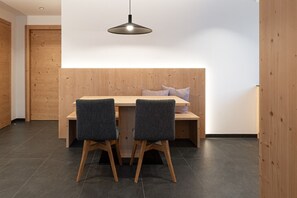 A modern dining area with a wooden table and two chairs, a bench with cushions, and a pendant light.