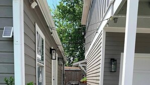 A narrow pathway leading to a wooden deck with potted plants and a small table. - Solace One | Lindale Park Houston (Houston)