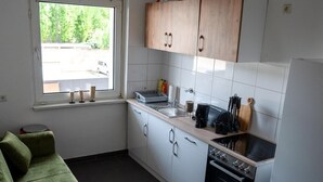 A compact kitchen with white cabinets, a built-in oven, and a window overlooking a street. - Livemore24 - Apartment 4 in Duisburg 24/7 check-in (Duisburg)