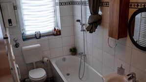 A bathroom with a toilet, a bathtub, a sink, and a window with blinds. - Livemore24 - Apartment 4 in Duisburg 24/7 check-in (Duisburg)