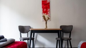 A room with a wooden table and two chairs, a red abstract painting on the wall, and a vase with dried flowers. - Livemore24 - Apartment 4 in Duisburg 24/7 check-in (Duisburg)