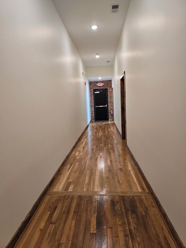 Un pasillo con suelo de madera, paredes blancas y una puerta negra con un rótulo que dice 'EXIT'.