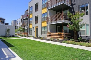 A modern multi-story residential building with balconies, a well-maintained lawn, and a small tree.