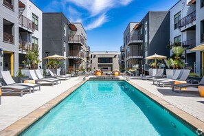 Ein moderner Poolbereich mit Liegestühlen und Sonnenschirmen, umgeben von mehrstöckigen Gebäuden mit Balkonen.