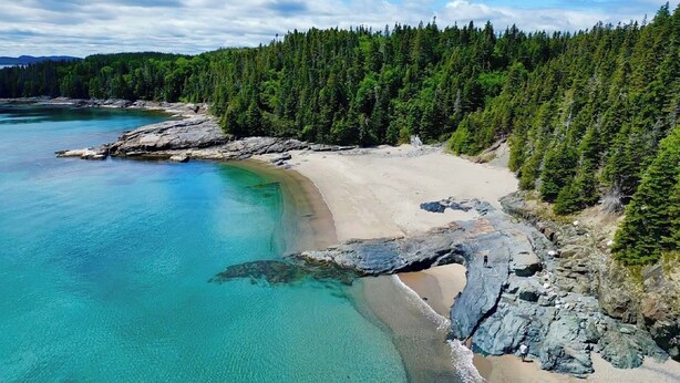 A coastal landscape with a sandy beach, clear turquoise waters, and dense forested hills. - Sandy Cove 04 Tucker Inn (Happy Adventure)