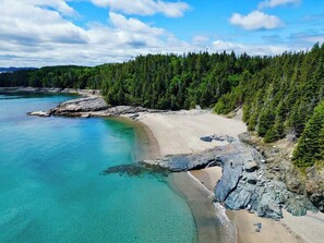 Paisatge costaner amb una platja sorrenca, aigües turqueses cristal·lines i turons boscosos i exuberants.